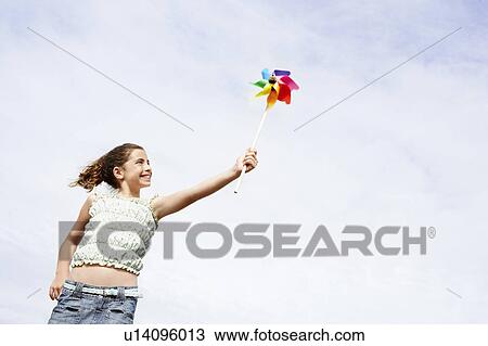 Stock Image - Smiling pre-teen Girl Holding Pinwheel above head, low angle view. Fotosearch