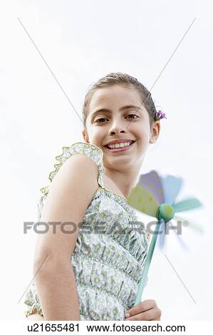 Stock Image - Smiling pre-teen girl holding pinwheel, low angle view. Fotosearch