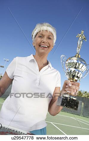 Smiling senior Woman holding Tennis Trophy on tennis court View Large Photo Image Stock Photo - Smiling senior Woman holding Tennis Trophy on tennis court. Fotosearch