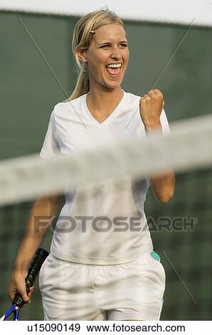 Stock Photo - Smiling Tennis Player Pumping Her Fist, standing near net. Fotosearch
