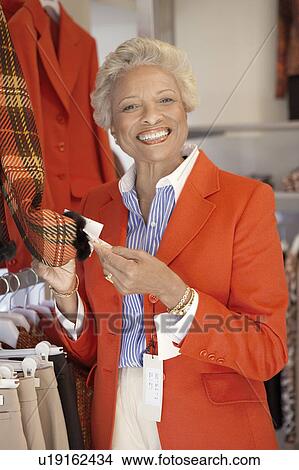 Picture - Smiling Woman checking price of blazer while Shopping. Fotosearch