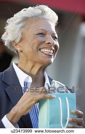 Smiling Woman standing outside holding Shopping Bag View Large Photo Image Stock Photo - Smiling Woman standing outside holding Shopping Bag. Fotosearch