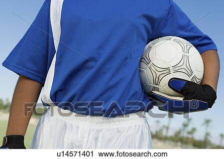 Stock Image - Soccer goalkeeper (13-17) holding ball, mid section. Fotosearch