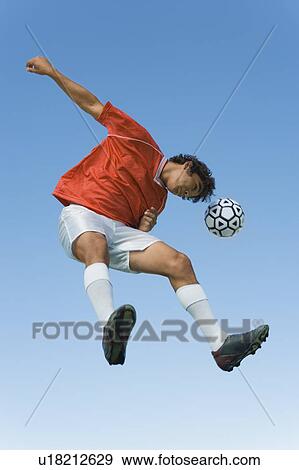 Stock Photo - Soccer player jumping to head the ball in mid-air with blue sky background. Fotosearch