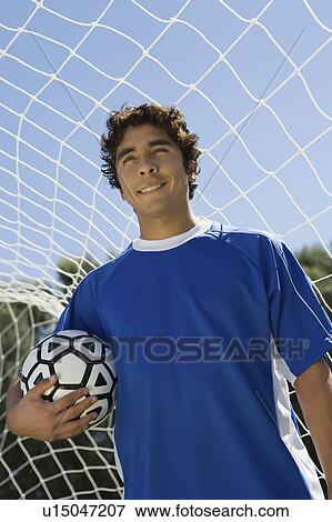 Stock Photo - Soccer player standing in goal holding ball, portrait. Fotosearch