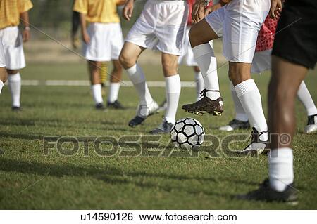 Stock Photograph - Soccer players competing for ball, low section. Fotosearch