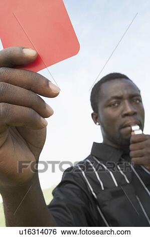 Stock Photograph - Soccer referee holding out red card and blowing whistle, portrait. Fotosearch