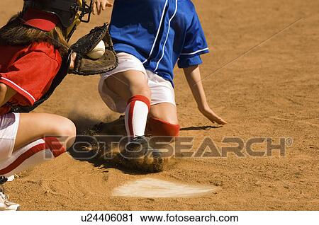 Stock Image - Softball player sliding into home plate, low section. Fotosearch