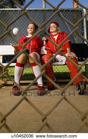 Stock Photograph - Softball players sitting on bench, front view. Fotosearch