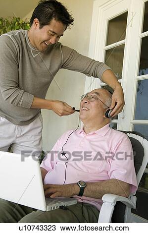 Stock Image - Son adjusting headset on father's head. Fotosearch