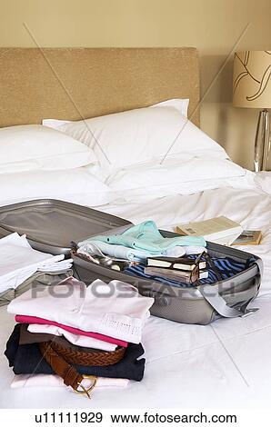 Stock Photo - Stacks of folded clothes and packed Suitcase on Bed. Fotosearch