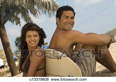 Stock Photo - Surfer couple sitting back to back against surfboard on beach. Fotosearch