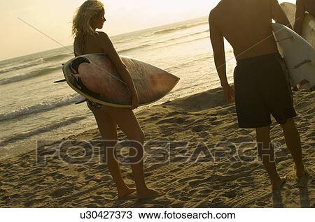 Surfers carrying surfboards on beach at sunset, back view View Large Photo Image Stock Image - Surfers carrying surfboards on beach at sunset, back view. Fotosearch