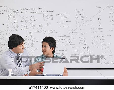 Stock Image - Teacher and student using laptop sitting in classroom. Fotosearch
