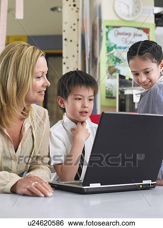 Stock Photograph - Teacher sitting with students using laptop in classroom. Fotosearch