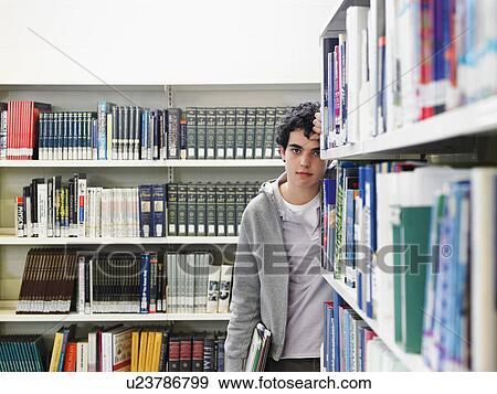 Stock Photo - Teenage boy leaning on bookshelf in library. Fotosearch