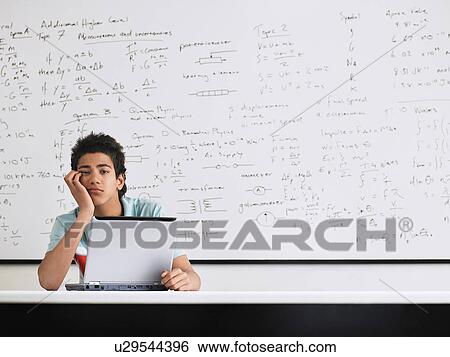 Stock Photograph - Teenage boy looking bored in front of whiteboard in classroom. Fotosearch