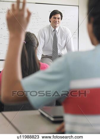 Stock Image - Teenage boy raising hand in classroom. Fotosearch