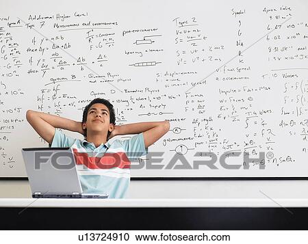 Stock Image - Teenage boy sitting in front of whiteboard in classroom. Fotosearch