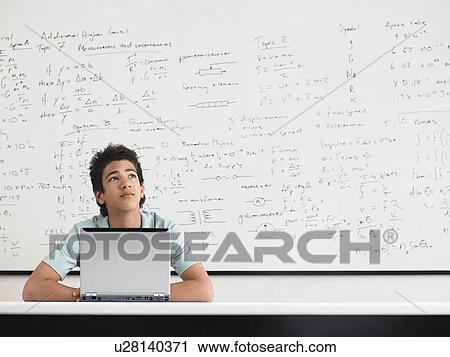 Stock Image - Teenage boy sitting in front of whiteboard in classroom. Fotosearch