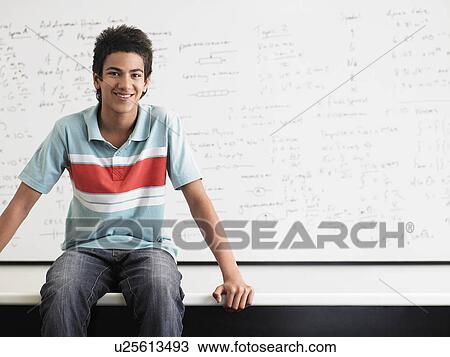 Teenage boy sitting on desktop in front of whiteboard View Large Photo Image Stock Image - Teenage boy sitting on desktop in front of whiteboard. Fotosearch