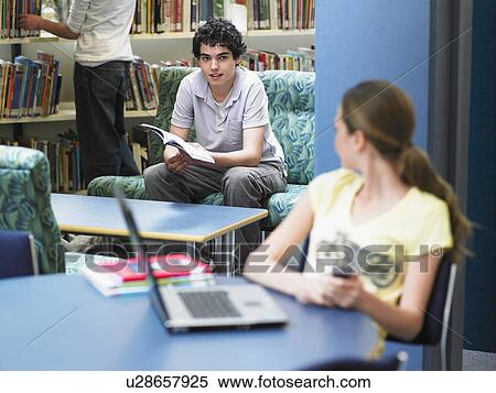 Stock Photography - Teenage girl looking at boy sitting in library. Fotosearch