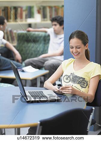 Stock Photo - Teenage girl texting sitting in library. Fotosearch