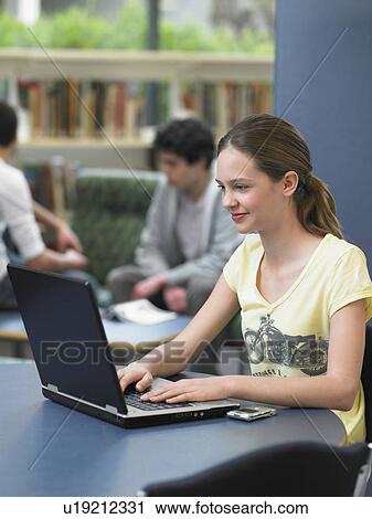 Stock Image - Teenage girl using laptop in library. Fotosearch