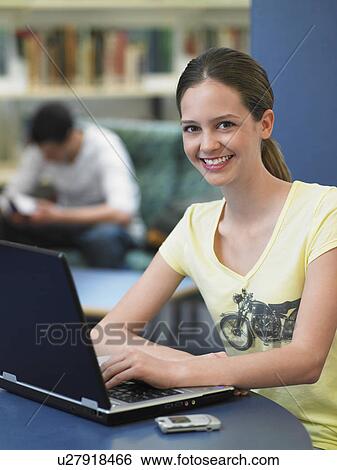 Stock Photograph - Teenage girl using laptop in library, portrait. Fotosearch