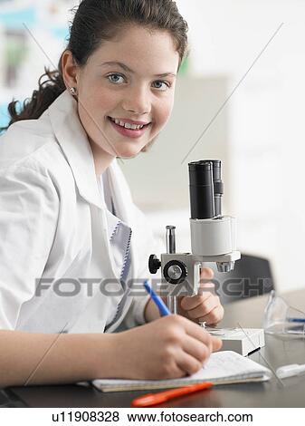 Stock Photo - Teenage girl using microscope and taking notes in classroom, portrait. Fotosearch