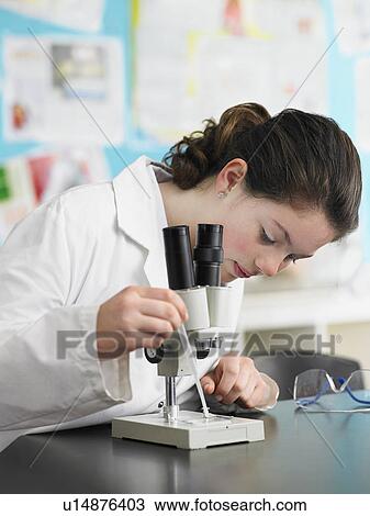 Stock Image - Teenage girl using microscope in classroom. Fotosearch