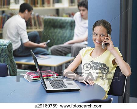 Stock Photo - Teenage using mobile phone sitting in library. Fotosearch