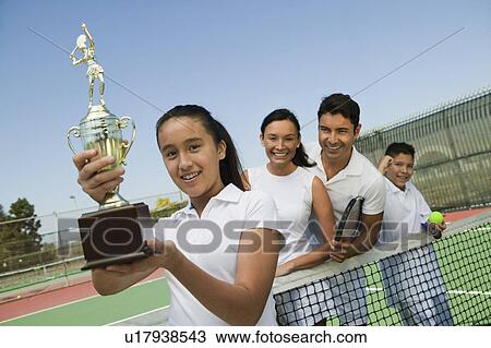 Stock Image - Tennis Family on court by net, daughter holding trophy, portrait. Fotosearch