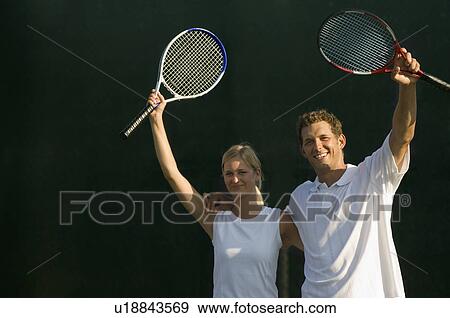 Stock Photo - Tennis Partners standing side by side, arms around, Raising Rackets in Victory. Fotosearch