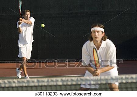 Tennis Player Hitting Backhand; doubles partner squatting at net View Large Photo Image Stock Image - Tennis Player Hitting Backhand; doubles partner squatting at net. Fotosearch