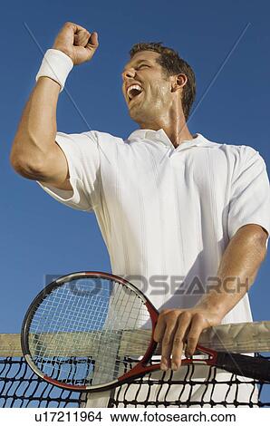 Picture - Tennis Player holding racket, standing at Net, pumping arm, low angle view. Fotosearch