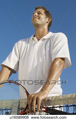 Stock Photograph - Tennis Player holding racket, standing at Net, low angle view. Fotosearch
