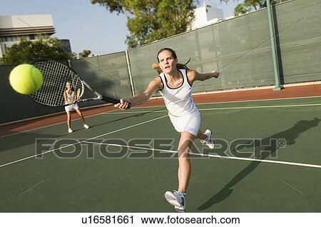 Stock Image - Tennis Player Reaching to hit tennis ball on tennis court. Fotosearch