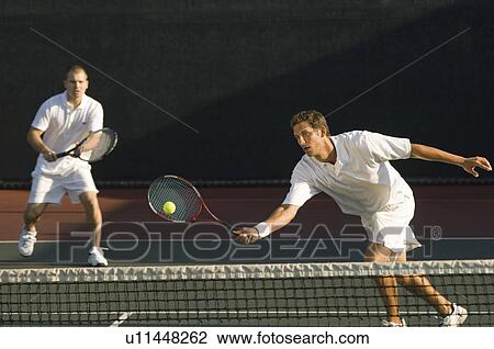 Tennis Player stretching, Swinging at Ball near tennis net, doubles partner standing behind View Large Photo Image Stock Image - Tennis Player stretching, Swinging at Ball near tennis net, doubles partner standing behind. Fotosearch
