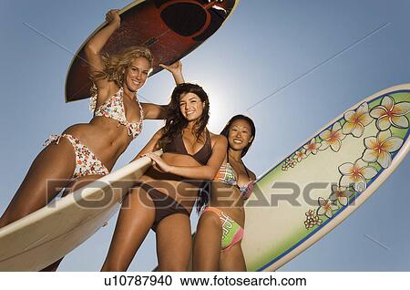 Three female surfers standing holding surfboards outdoors, low angle view View Large Photo Image Stock Image - Three female surfers standing holding surfboards outdoors, low angle view. Fotosearch