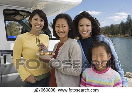 Stock Photo - Three-generation of women eating breakfast outside of RV at lake. Fotosearch