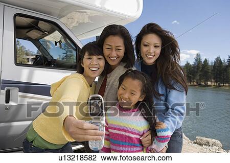 Stock Image - Three-generations of women photographing selves outside RV at lake. Fotosearch