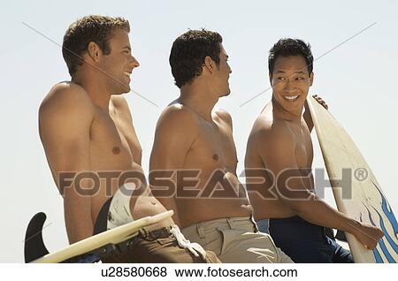 Stock Photo - Three surfers sitting holding surfboards outdoors. Fotosearch