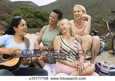 Stock Photo - Three women singing with guitar player on beach. Fotosearch