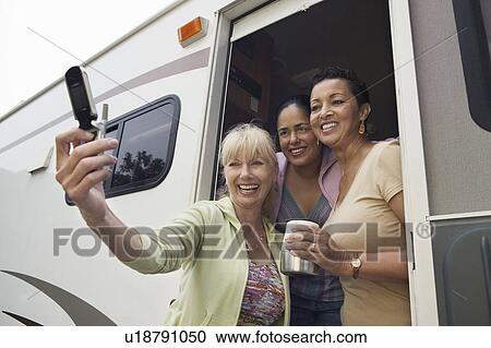 Stock Image - Three women using camera phone in motor home. Fotosearch
