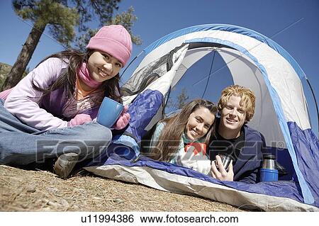 Stock Photograph - Three young adults at campsite by tent at campsite. Fotosearch