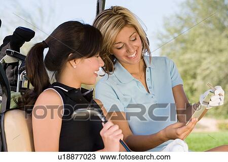 Stock Image - Two female golfers reading notes while sitting in golf cart. Fotosearch