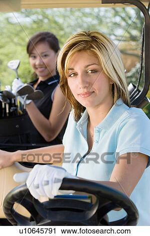 Stock Image - Two female golfers sitting in golf cart. Fotosearch