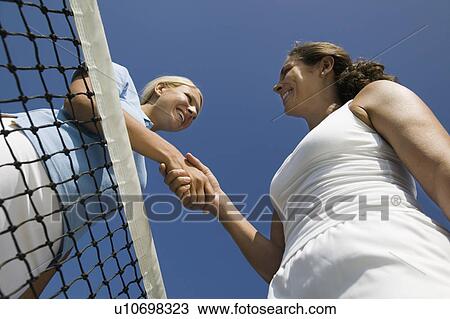 Stock Image - Two female Tennis Players shaking hand over tennis court net, low angle view. Fotosearch