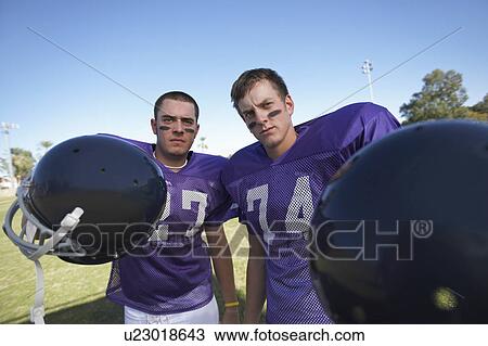 Stock Image - Two Football Players Holding Helmets on field, portrait. Fotosearch